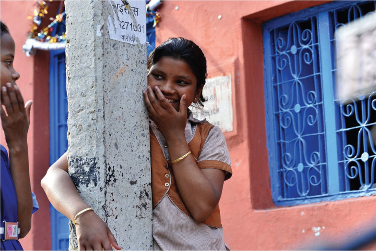 A schoolgirl smiling beside a pillar outside a building